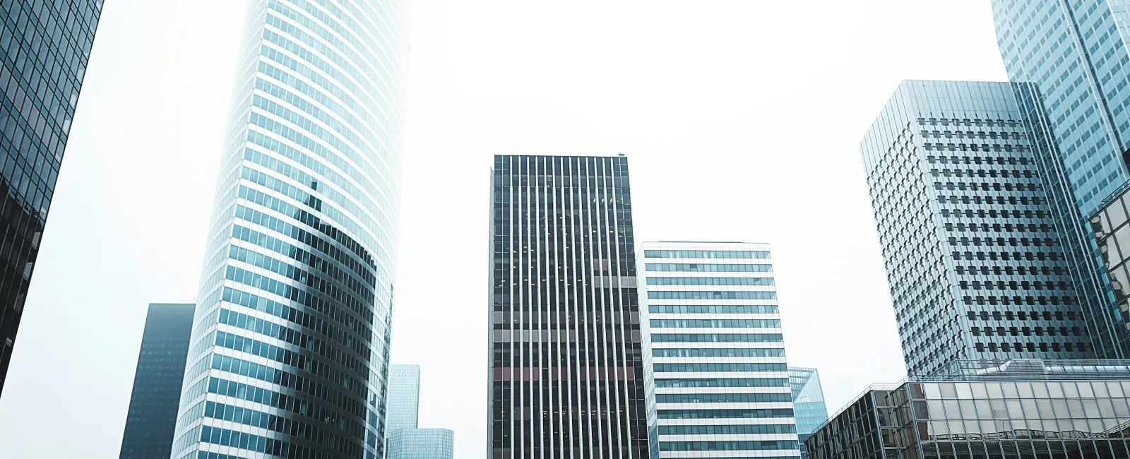Modern glass skyscrapers rising in a city with bright overcast sky and reflections on building surfaces.