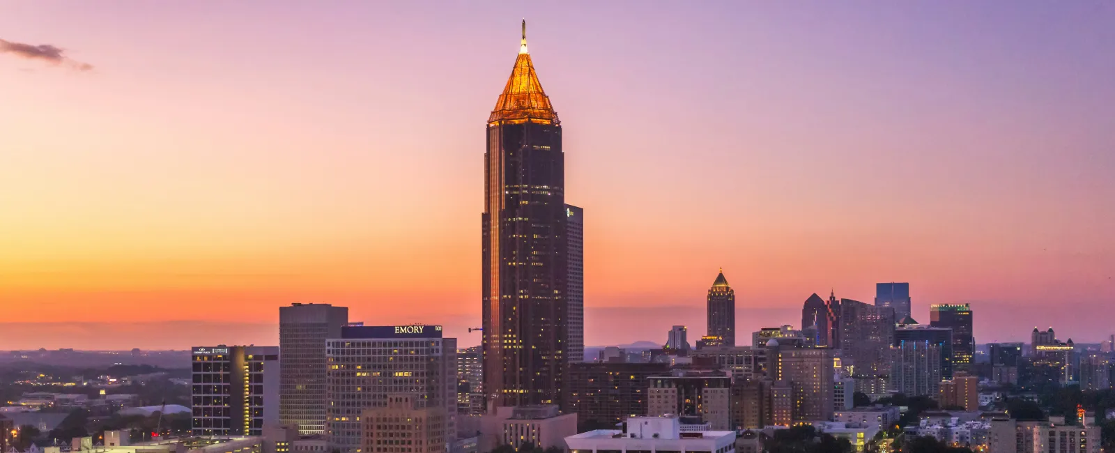 Atlanta skyline at sunset with Bank of America Plaza lit up against a colorful sky.