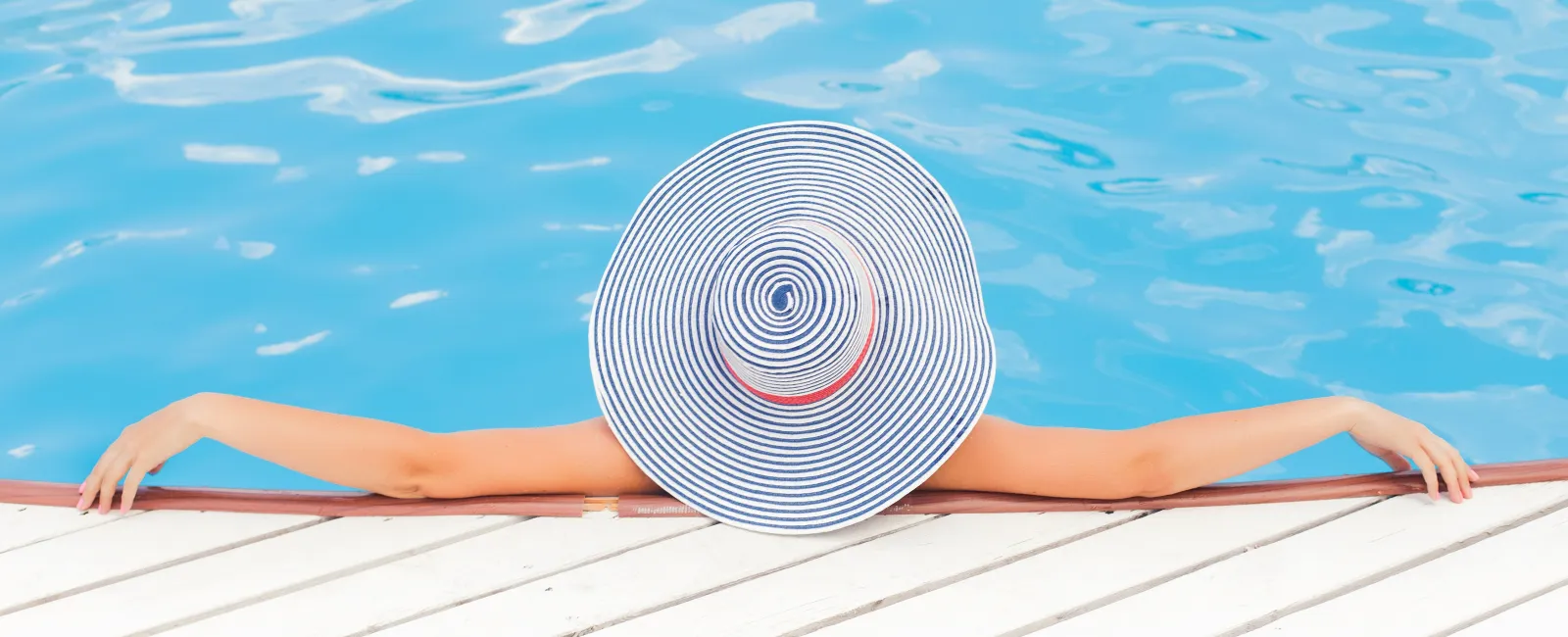 A person relaxing by a swimming pool, wearing a wide-brimmed striped hat, enjoying the sunshine.