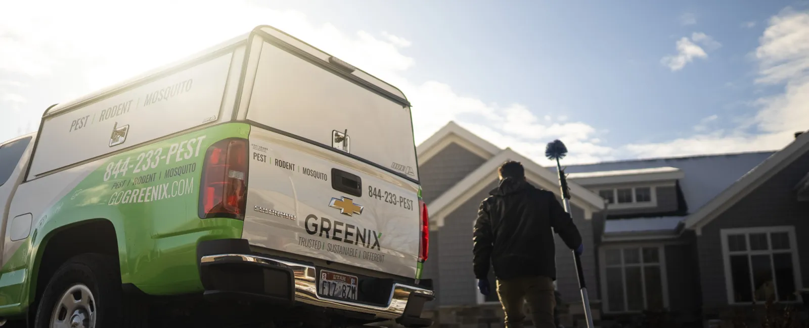 Greenix pest control truck parked outside a house with technician walking towards home holding equipment in winter.