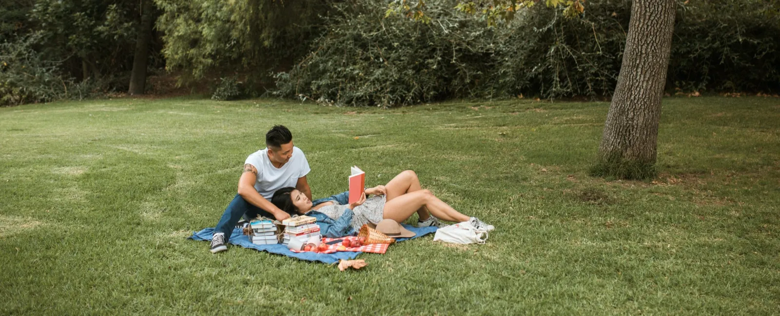 a man and woman sitting on a blanket in a grassy area