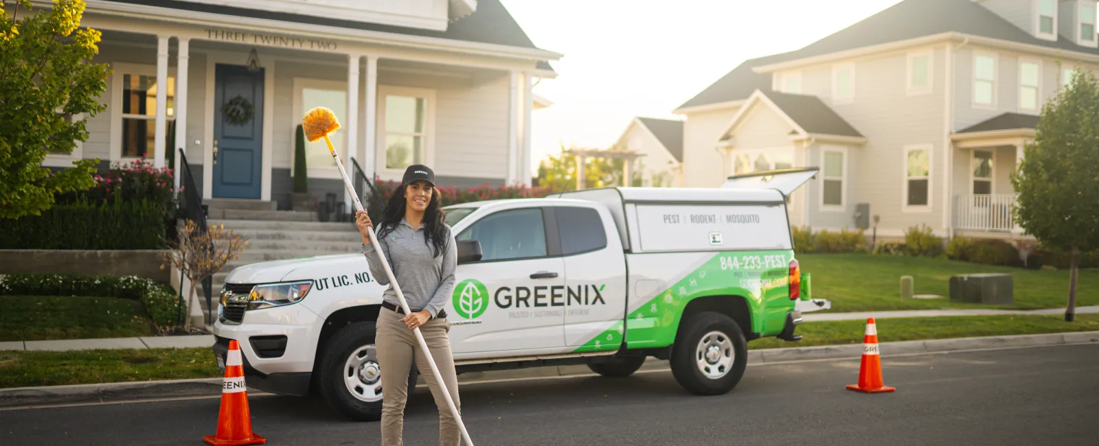 Woman with cleaning equipment standing in front of a Greenix pest control truck on a suburban street.