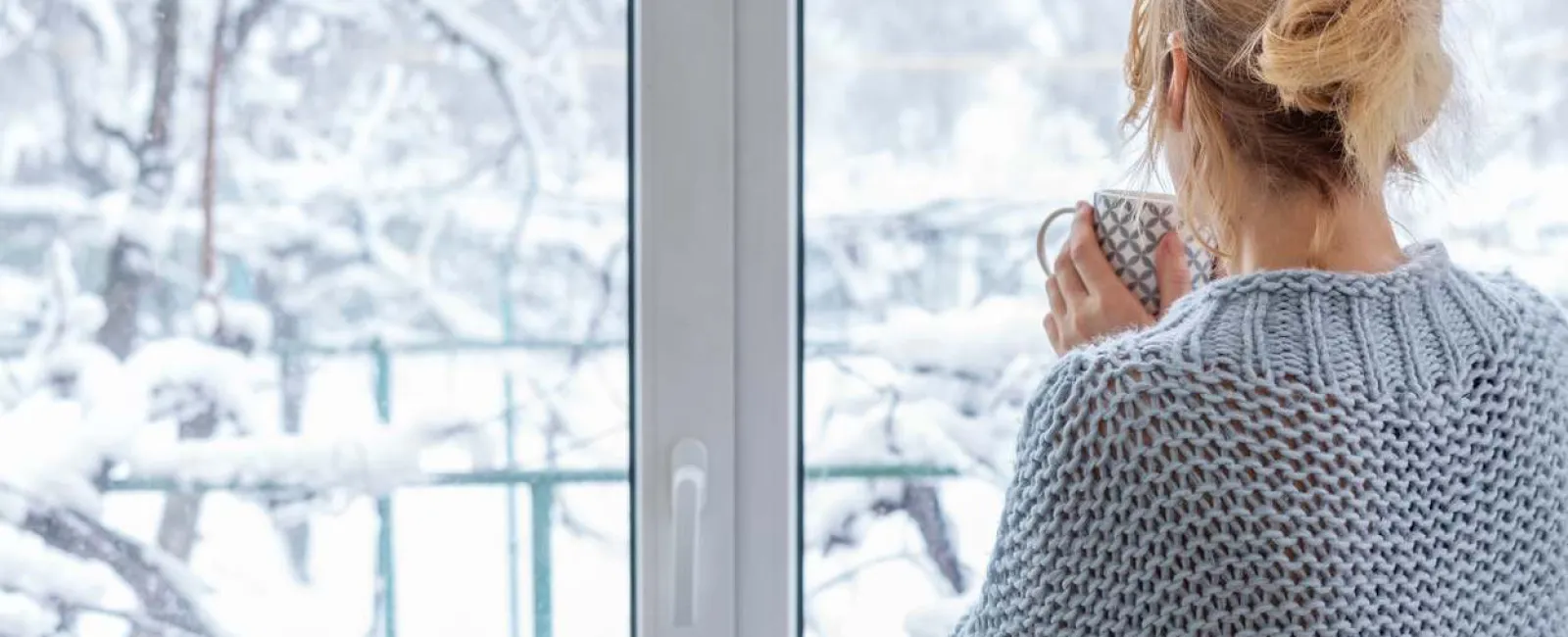 a woman looking out of a window into the snow while holding a cup