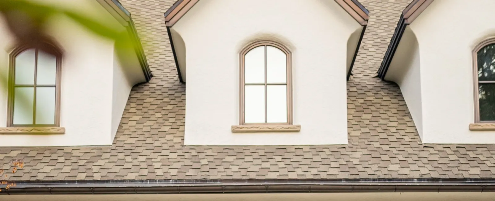 Worker cleaning exterior wall light fixtures on a beige house with three dark garage doors and arched windows.