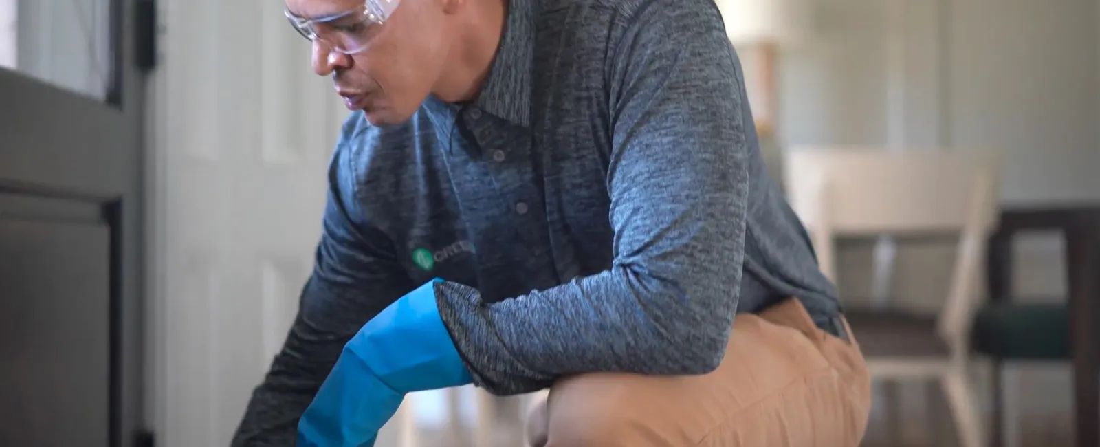 Man wearing protective gloves and safety glasses inspecting a door frame in a home interior.