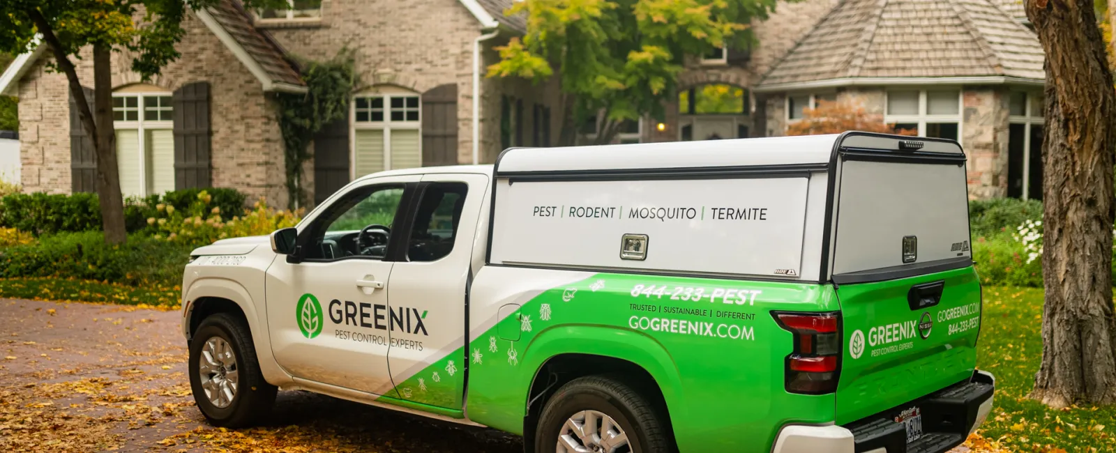 Greenix pest control truck parked in a residential driveway during autumn with home and trees in background.