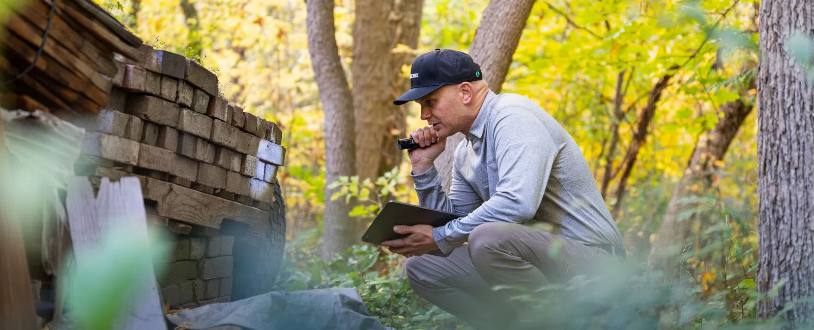 A man in a gray sweatshirt examines a wooden structure in a vibrant autumn forest.