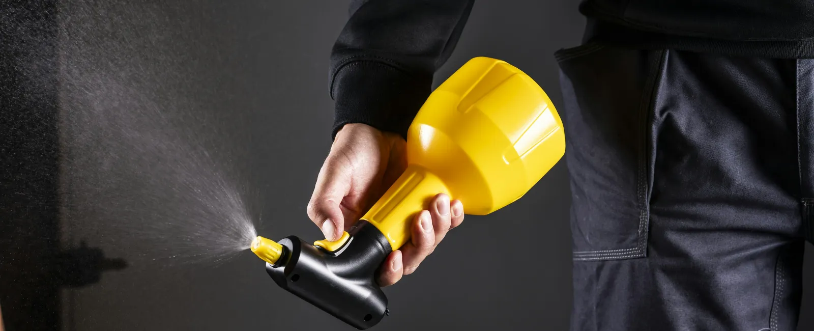 Person holding a yellow spray nozzle releasing a fine mist against a dark background.