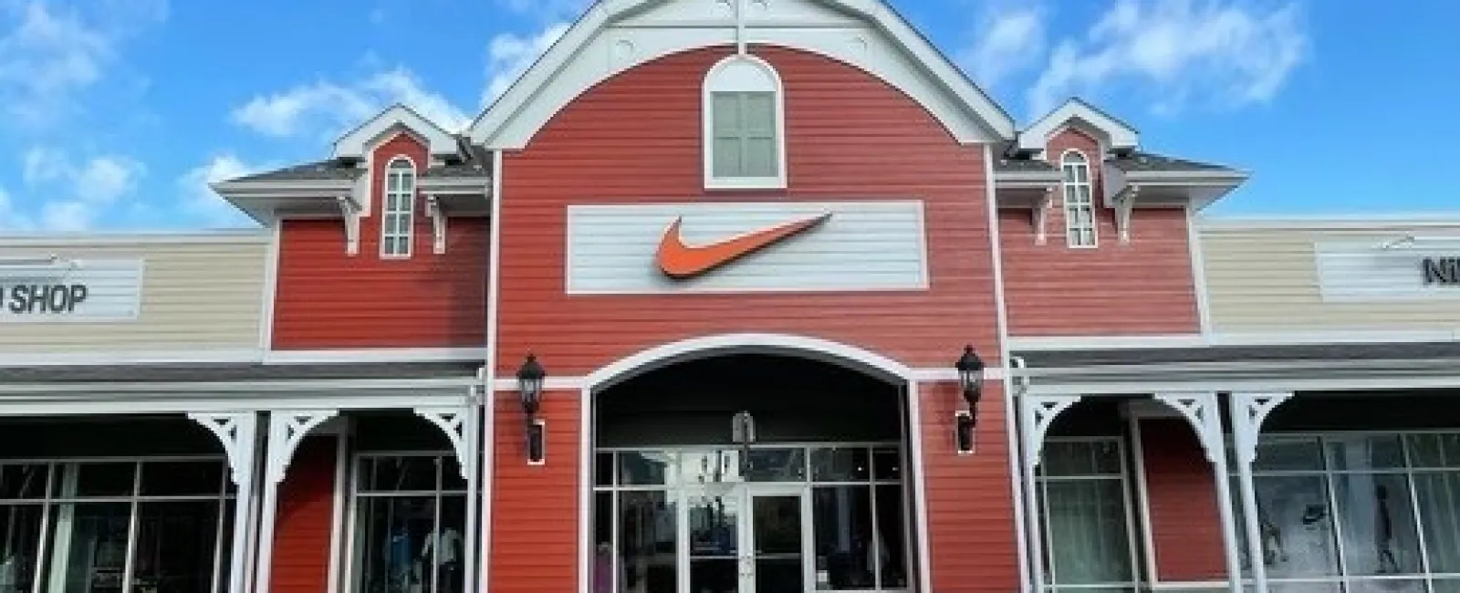 Exterior of a red and beige Nike store with a large orange swoosh logo under a blue sky