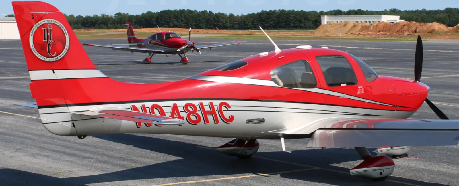 Red and white single-engine airplane parked on runway with another plane in the background on a clear day