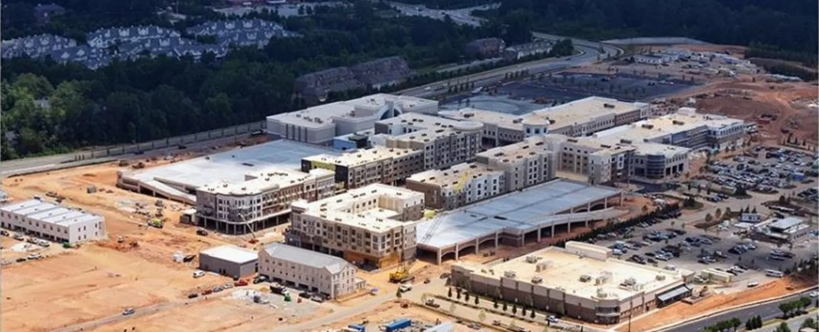 Aerial view of a large construction site with multiple buildings under development and surrounding forest area.