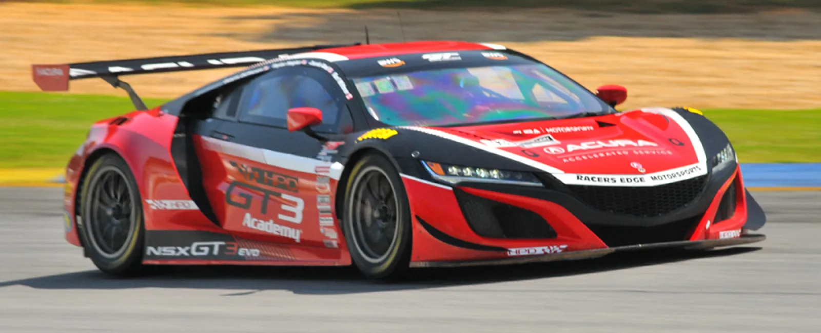 Red and black NSX GT3 Evo race car speeding on a race track during a motorsport event.