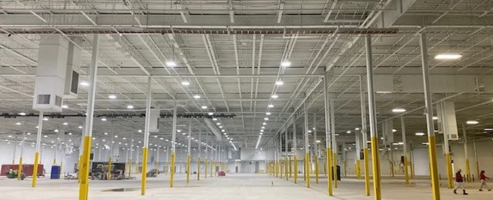 Wide interior of an empty warehouse with yellow support columns and bright overhead lighting