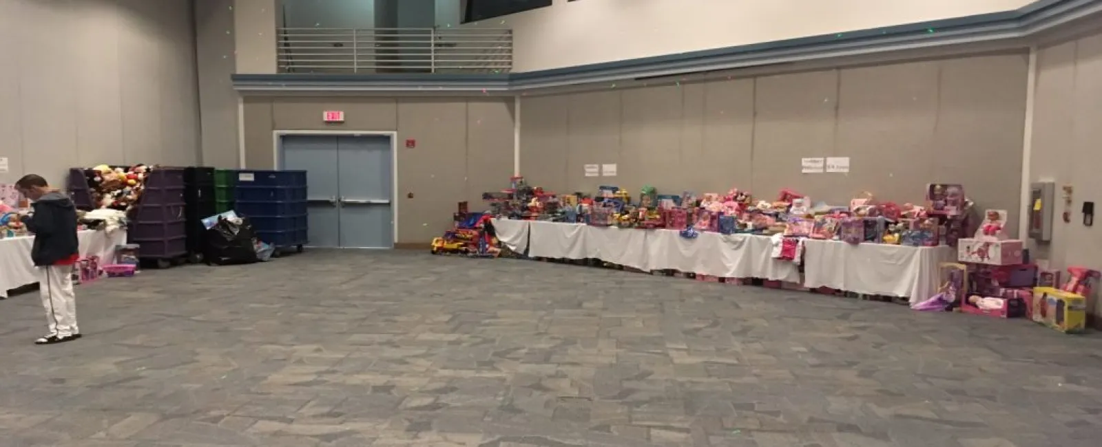 Large room with tables lined with toys and gifts along the walls, a child standing near the toys.