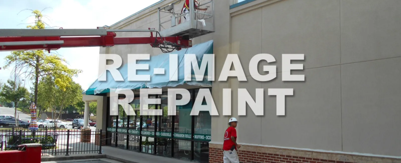 Workers repainting the exterior wall of a commercial building using a lift and paint supplies outdoors.