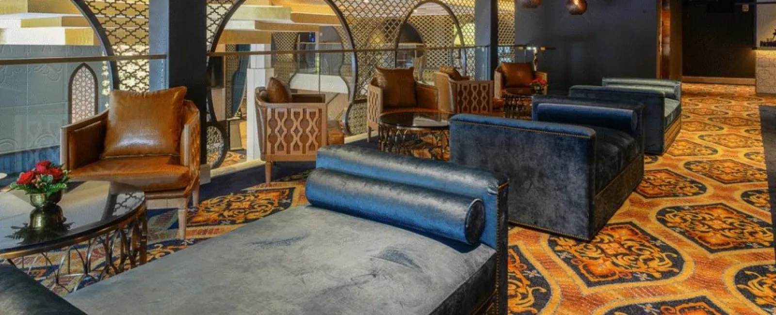 Luxury lounge area with plush blue sofas, leather armchairs, ornate carpet, and decorative lighting.