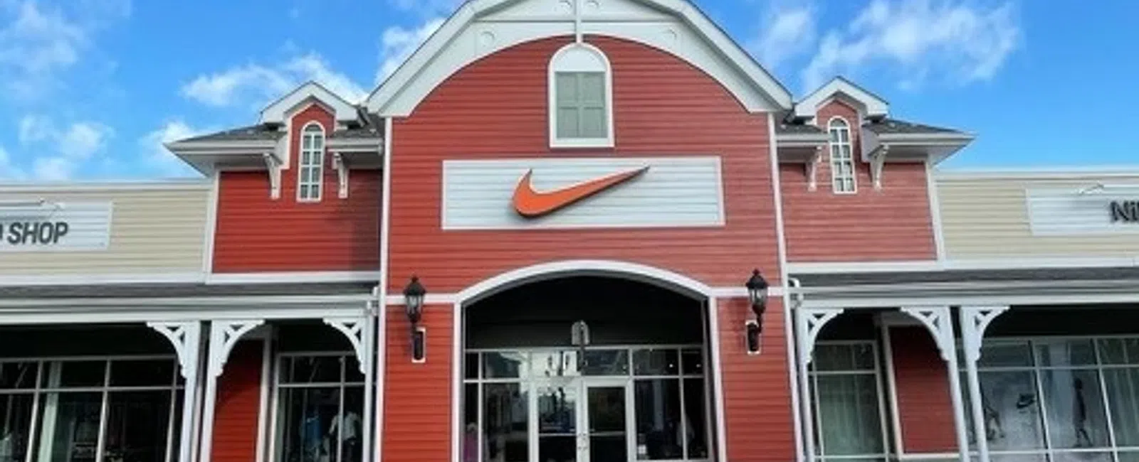 Exterior of a red and beige Nike store with a large orange swoosh logo under a blue sky