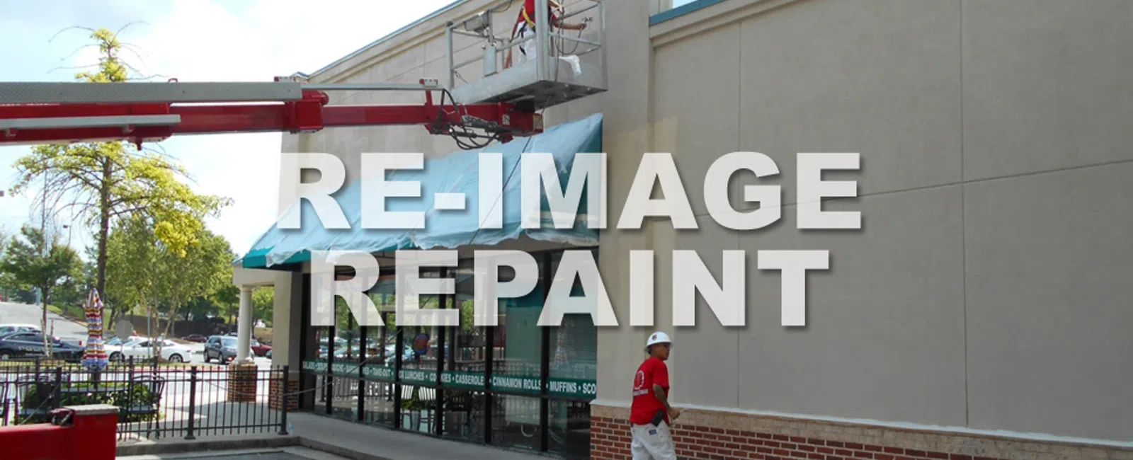 Workers repainting the exterior wall of a commercial building using a lift and paint supplies outdoors.