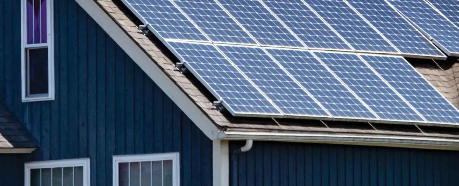 Solar panels installed on the roof of a modern blue house under clear daylight sky.