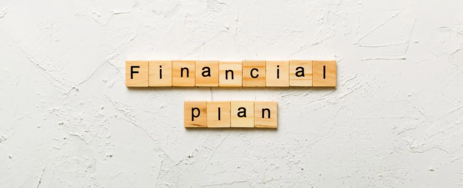 Wooden letter tiles spelling financial plan on a textured white background representing money management.