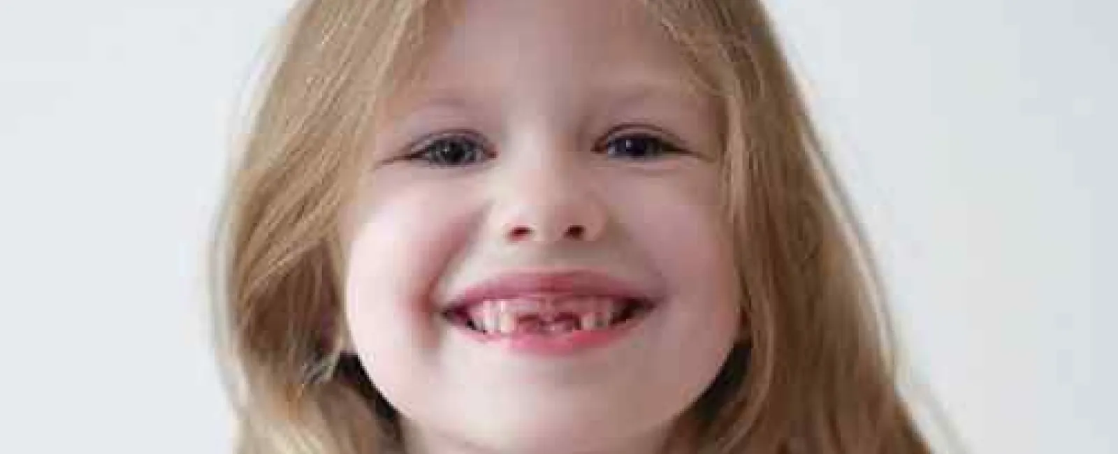Smiling young girl with missing front teeth holding a fan of US dollar bills against a plain background
