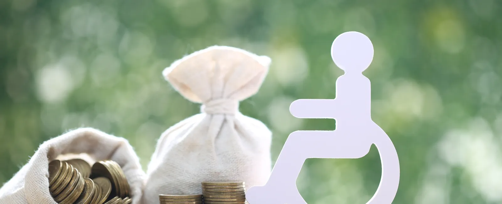 Stacks of coins and money bags beside a white wheelchair accessibility symbol on a bright background.