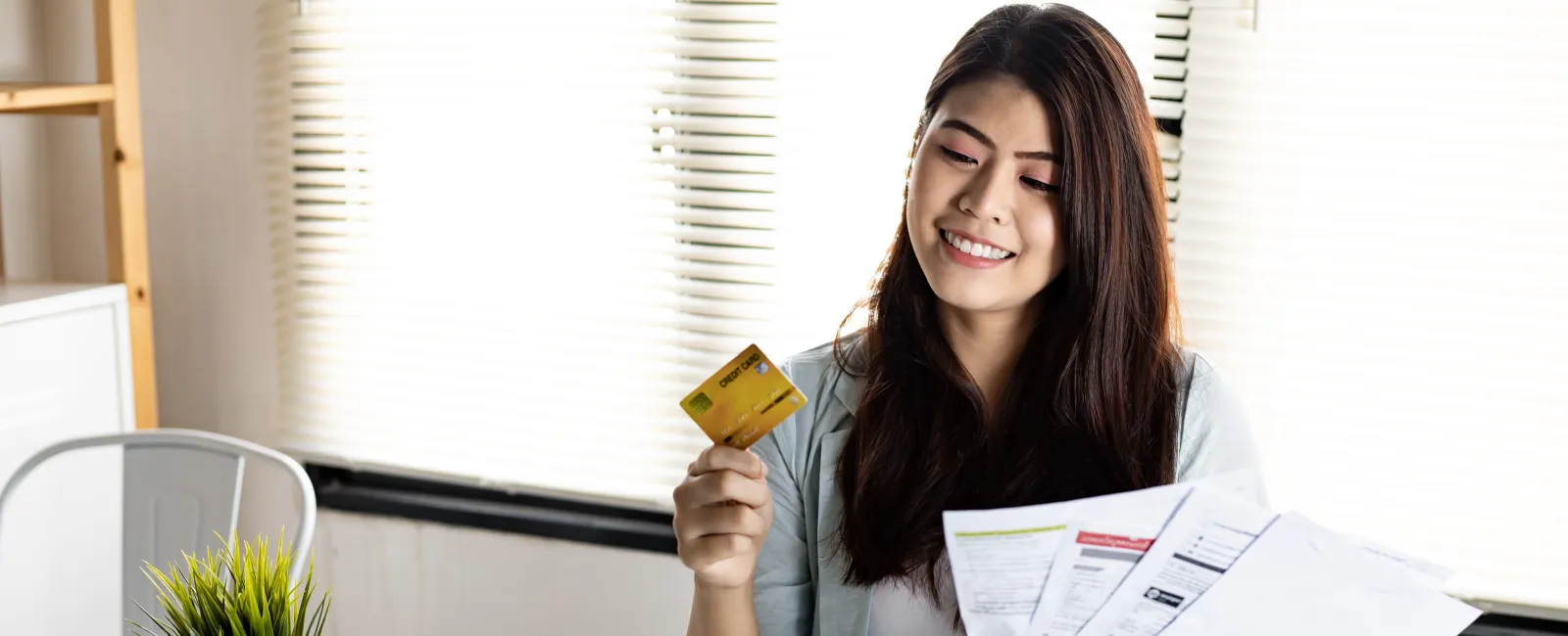 Happy woman reviewing bills while holding a credit card at a desk with a laptop and notebook.