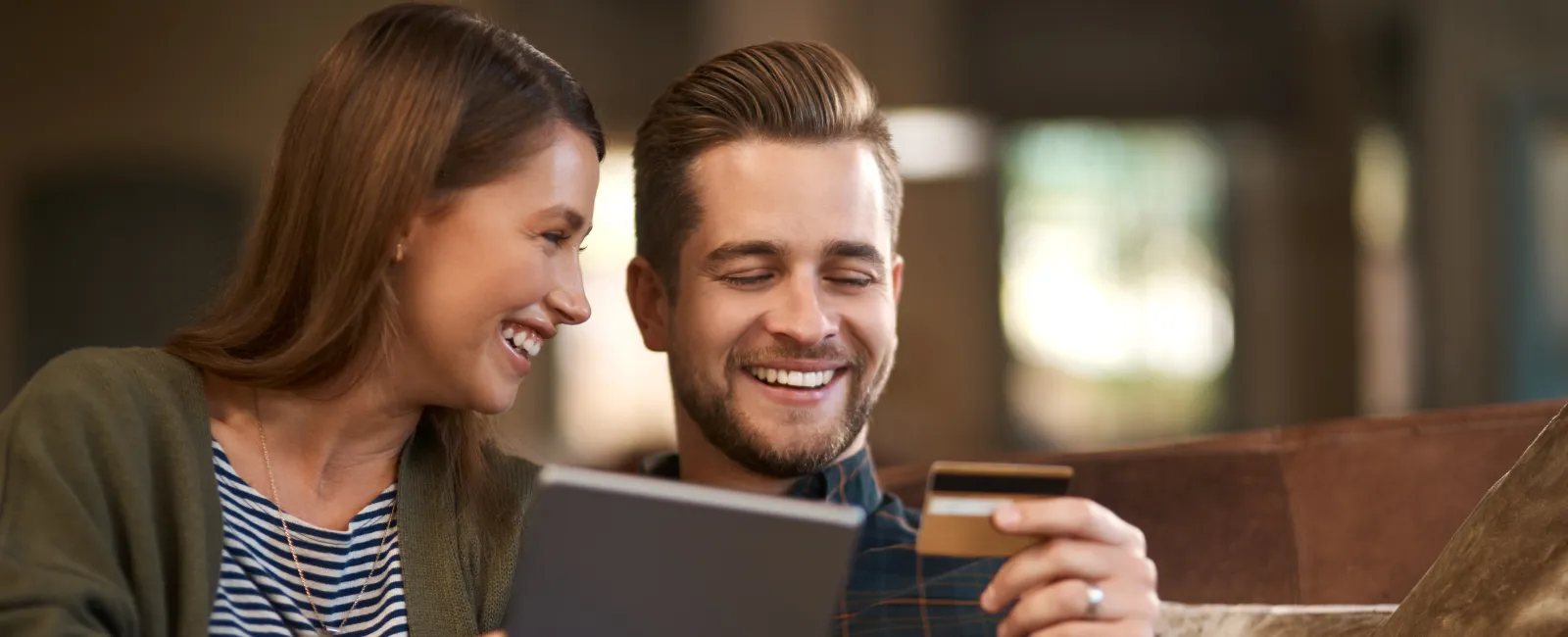 Happy couple shopping online using tablet and credit card on a cozy couch at home