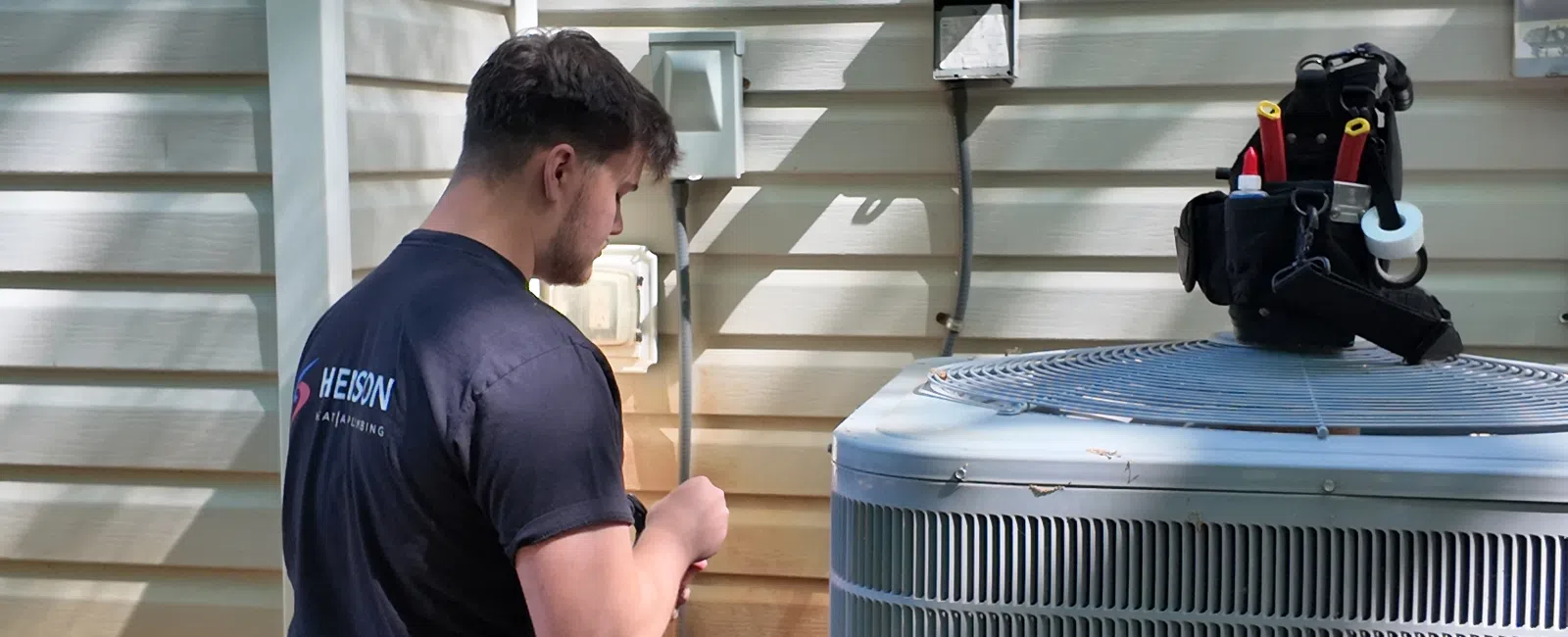 Technician kneeling beside a Carrier air conditioning unit outside a house during repair work.