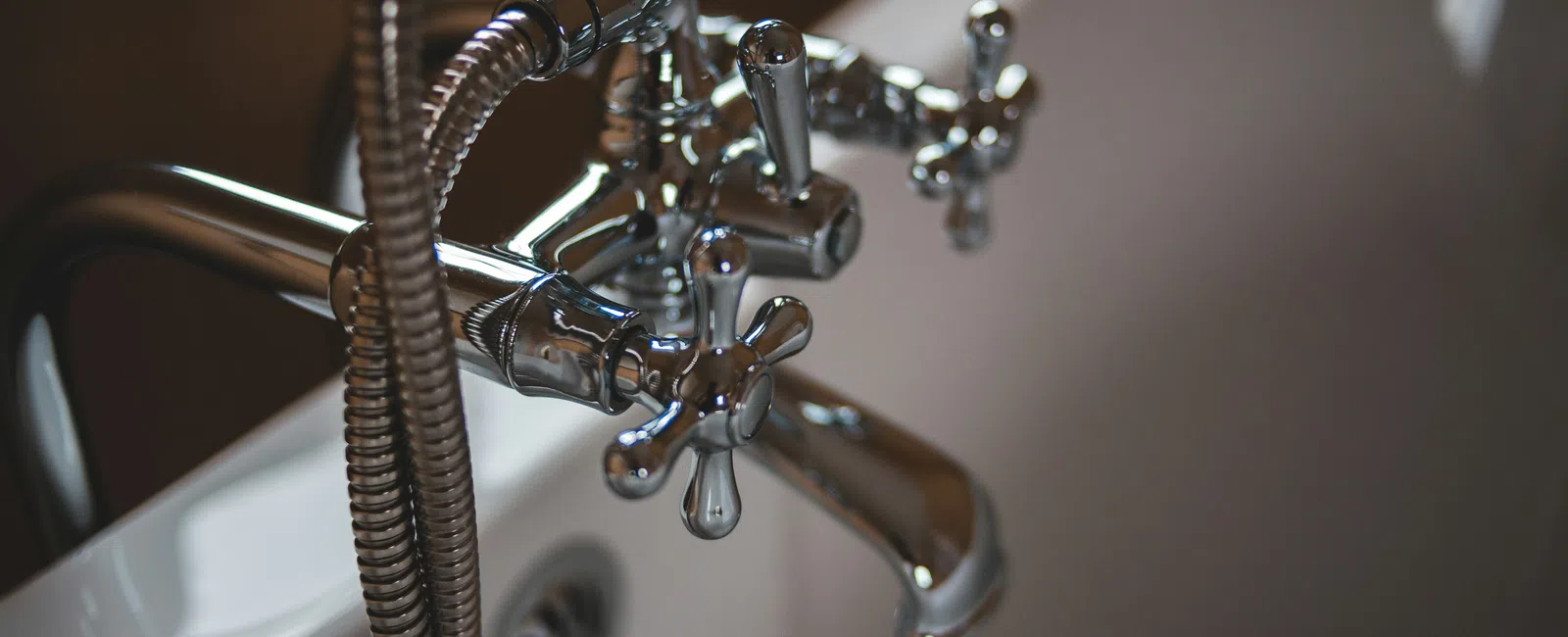 Close-up of vintage chrome bathtub faucet and flexible shower hose on white porcelain tub.