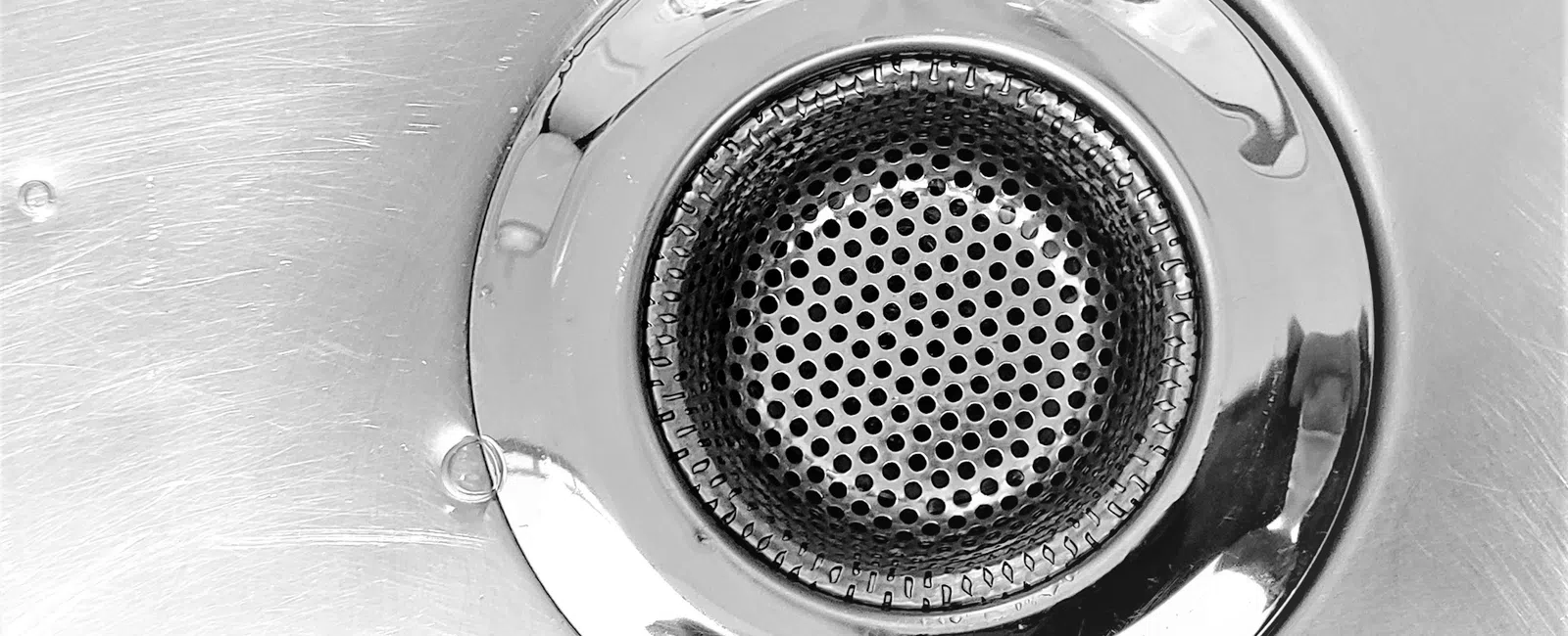 Close-up of a shiny metal sink drain with perforated strainer and brushed steel surface