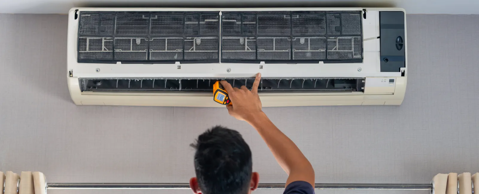 Technician inspecting and repairing a wall-mounted air conditioner unit indoors using a handheld tool.