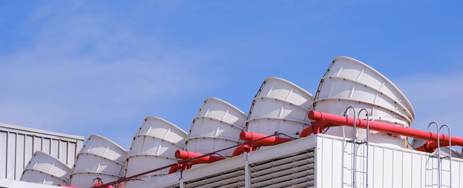 Row of large white industrial ventilation fans with red pipes on a rooftop against a blue sky.