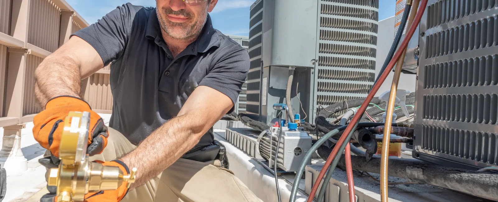 HVAC technician in safety gear working on air conditioning units on rooftop under clear sky