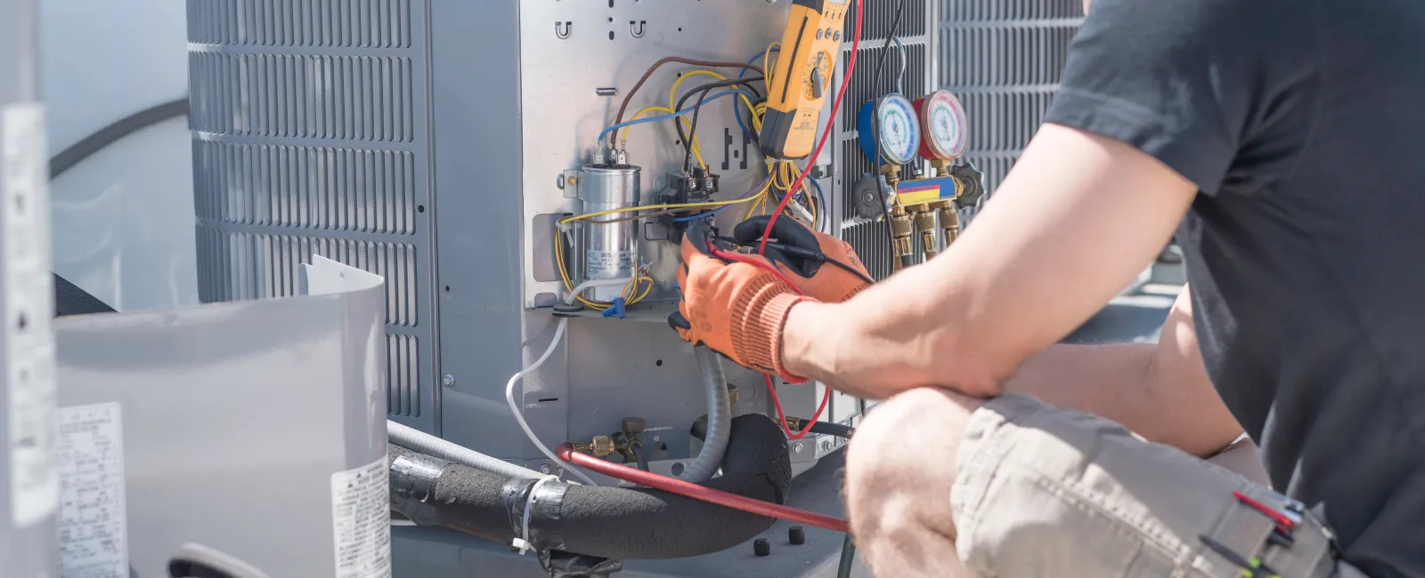 Technician wearing gloves repairing an outdoor HVAC unit using electrical tools on a sunny day.