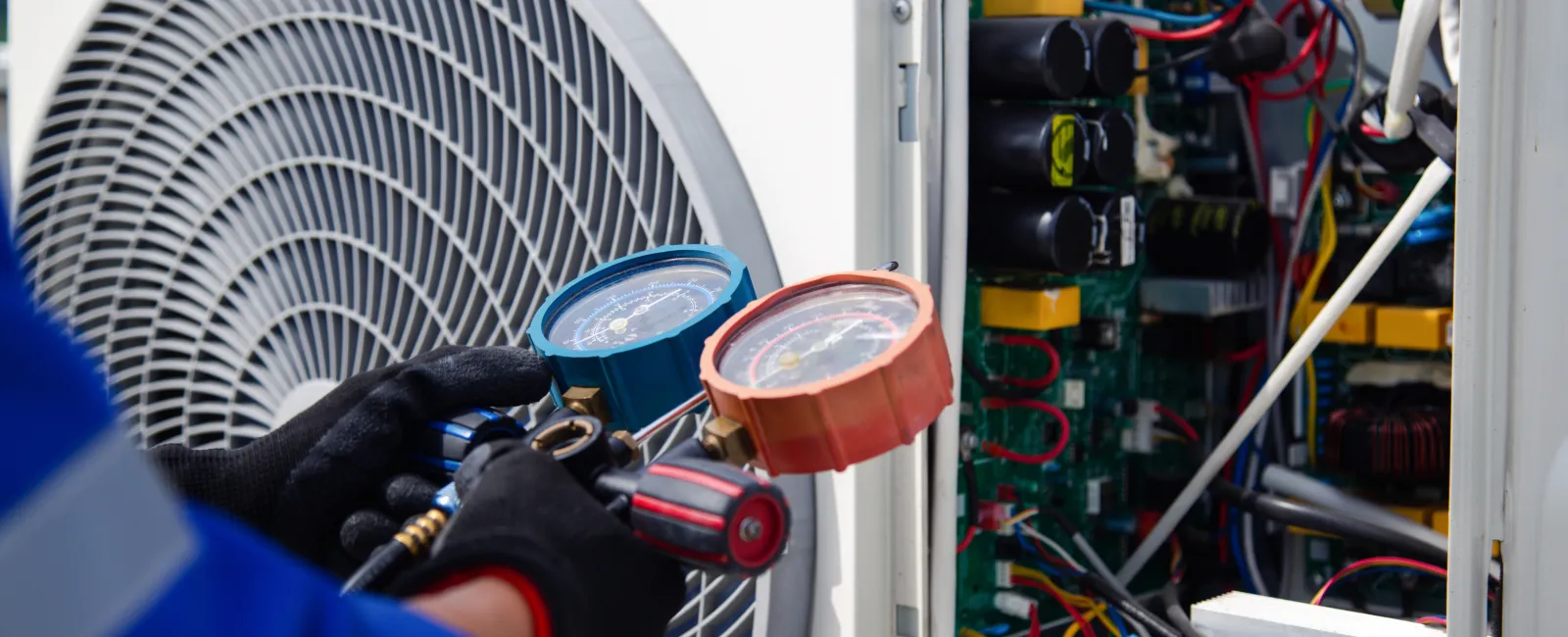 Technician in gloves using gauges to check and repair an air conditioning unit's electrical components.