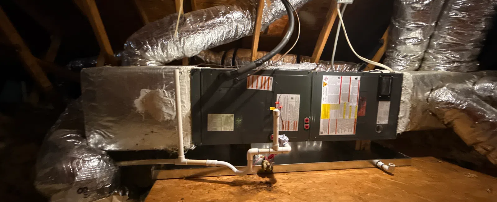 HVAC system with insulated ductwork and pipes installed in a wooden attic space under roof beams.