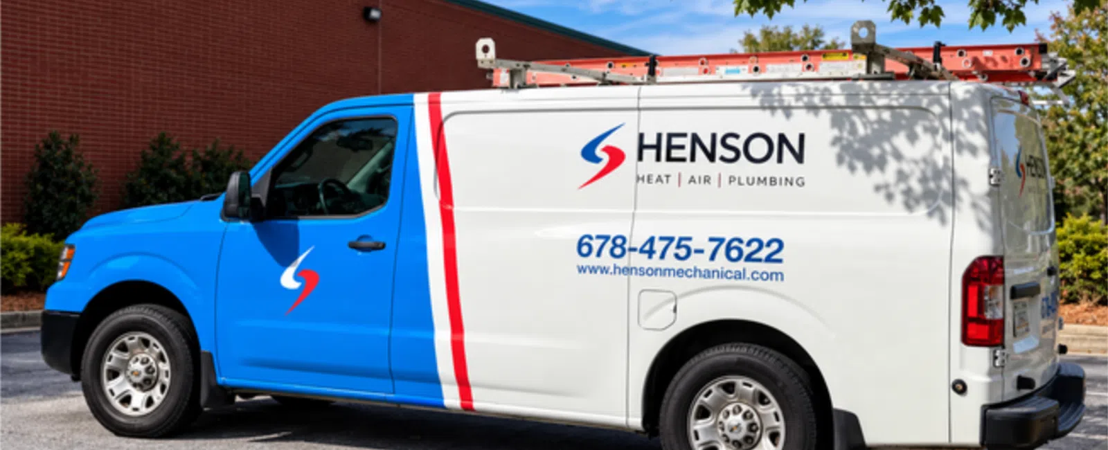 Blue and white Henson service van with logo, contact number, and ladder on top parked by a red brick building.