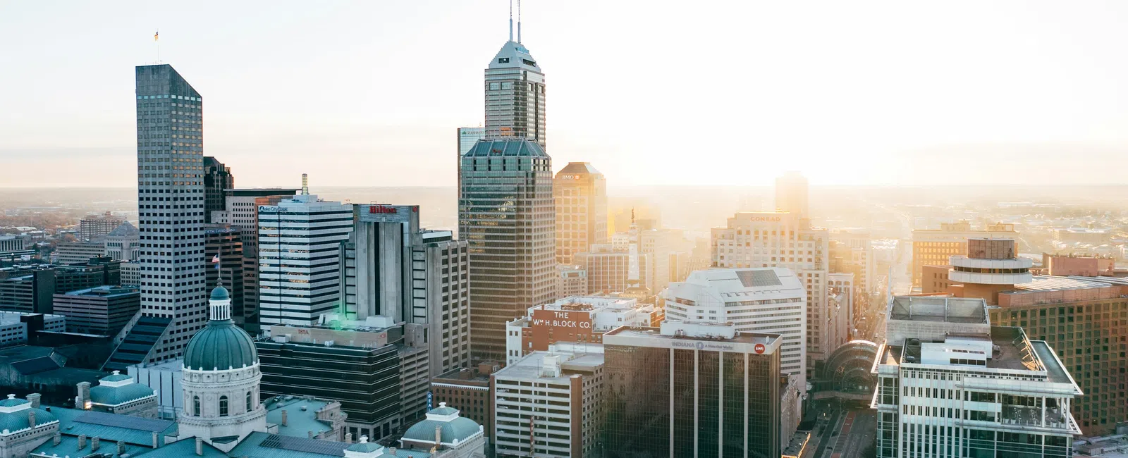 Sunlit skyline of a modern city with tall skyscrapers and historic buildings at sunrise.