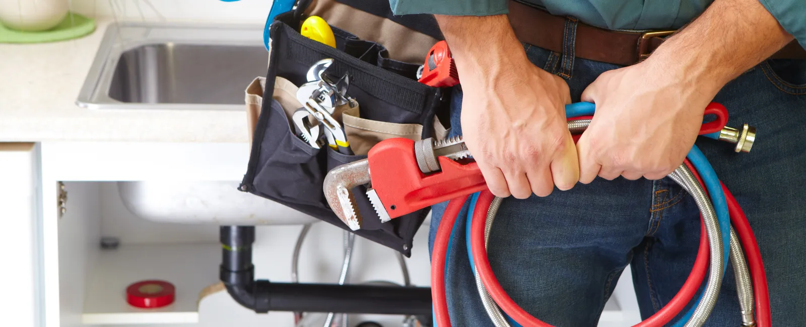 A plumber holding tools and hoses in a kitchen during a repair service.