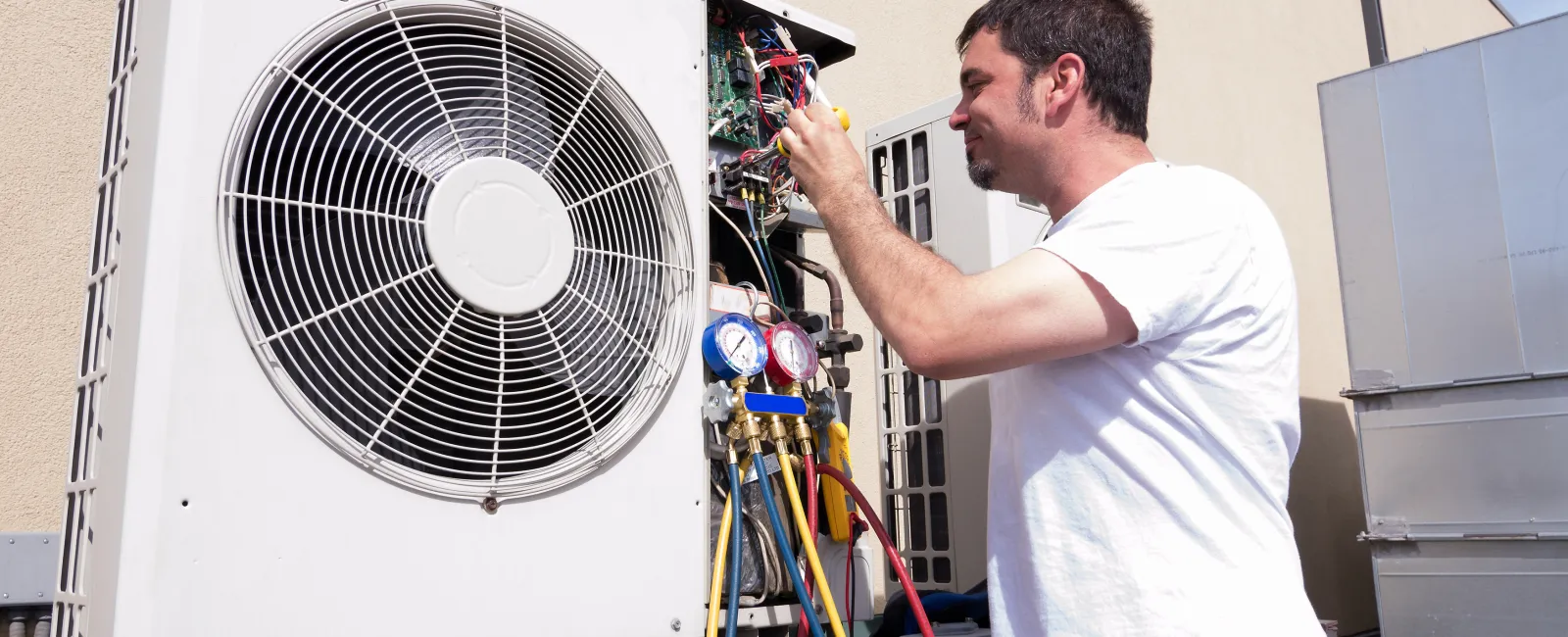 Technician repairing and servicing outdoor air conditioning unit with gauges and tools on a sunny day