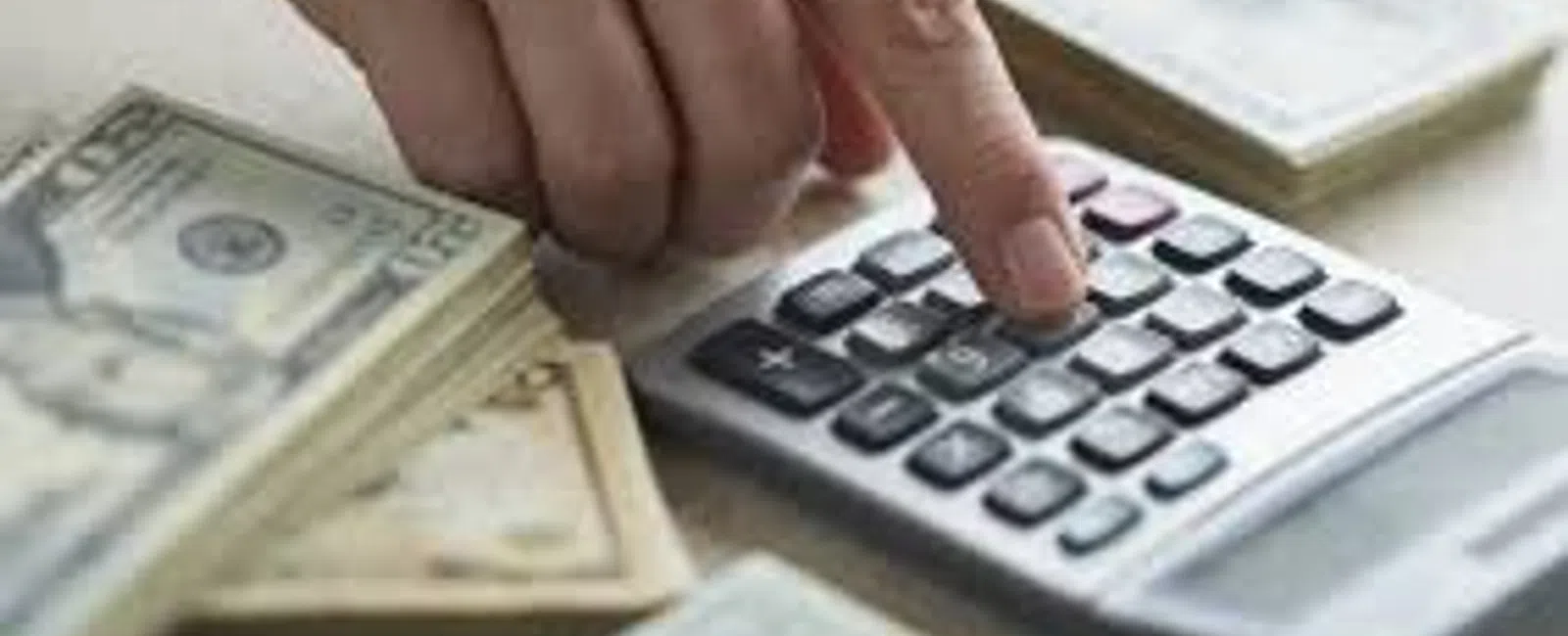 Hand pressing calculator buttons with stacks of US dollar bills on the table for financial calculations.