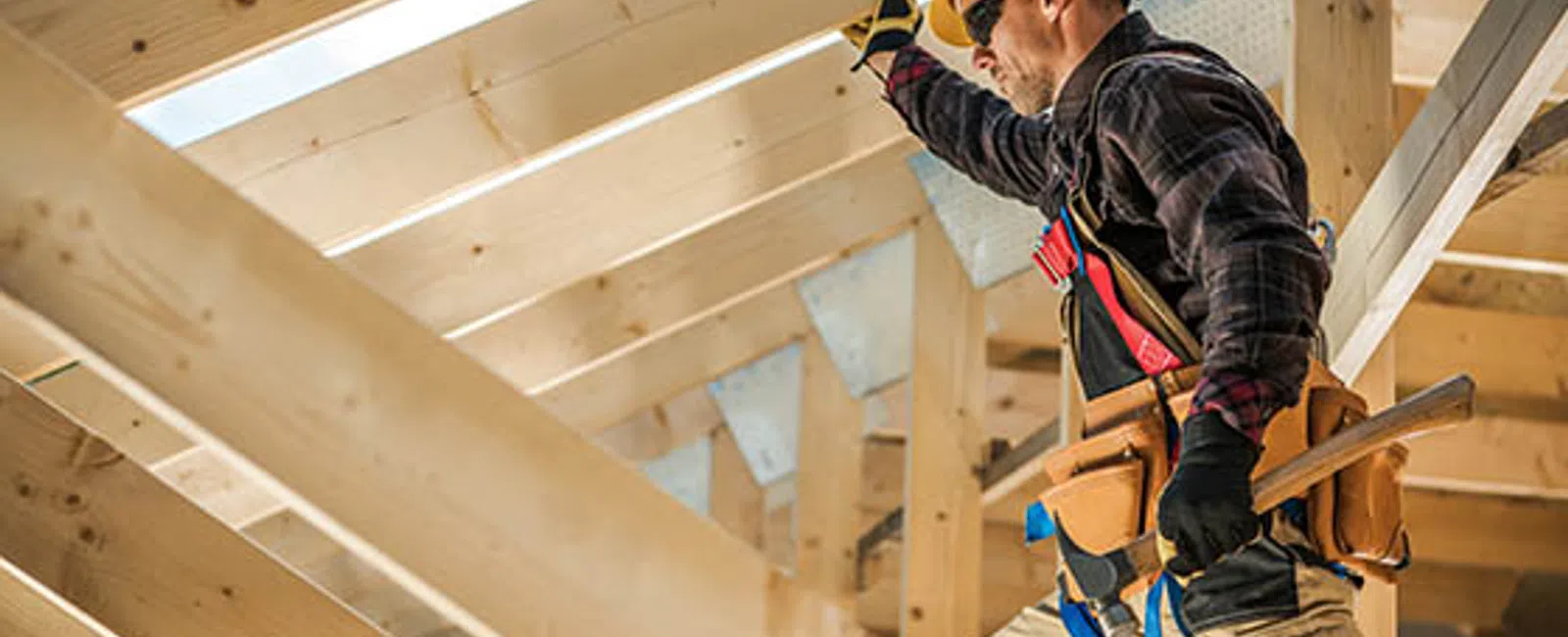 Construction worker wearing safety gear inspecting wooden roof framing on construction site