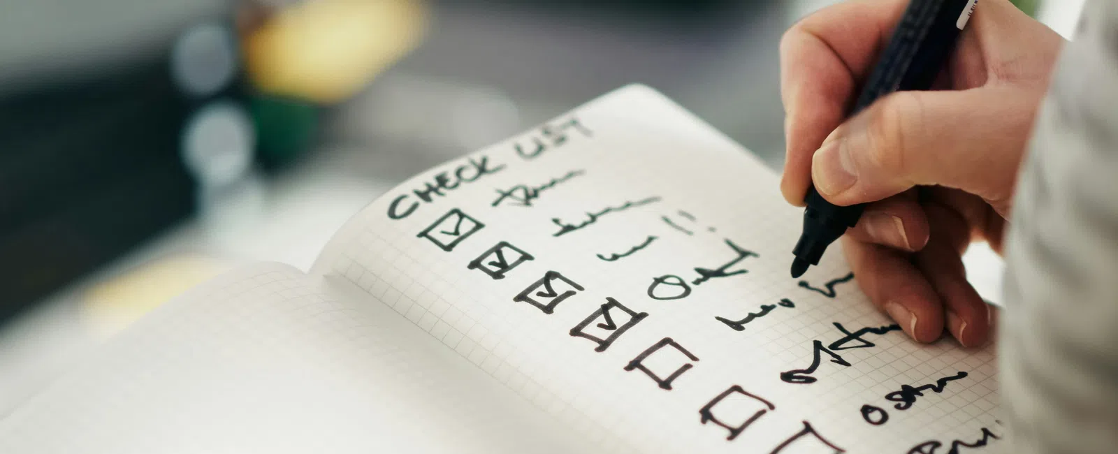 Hand writing on a checklist notebook with multiple items checked and some unchecked in black ink.