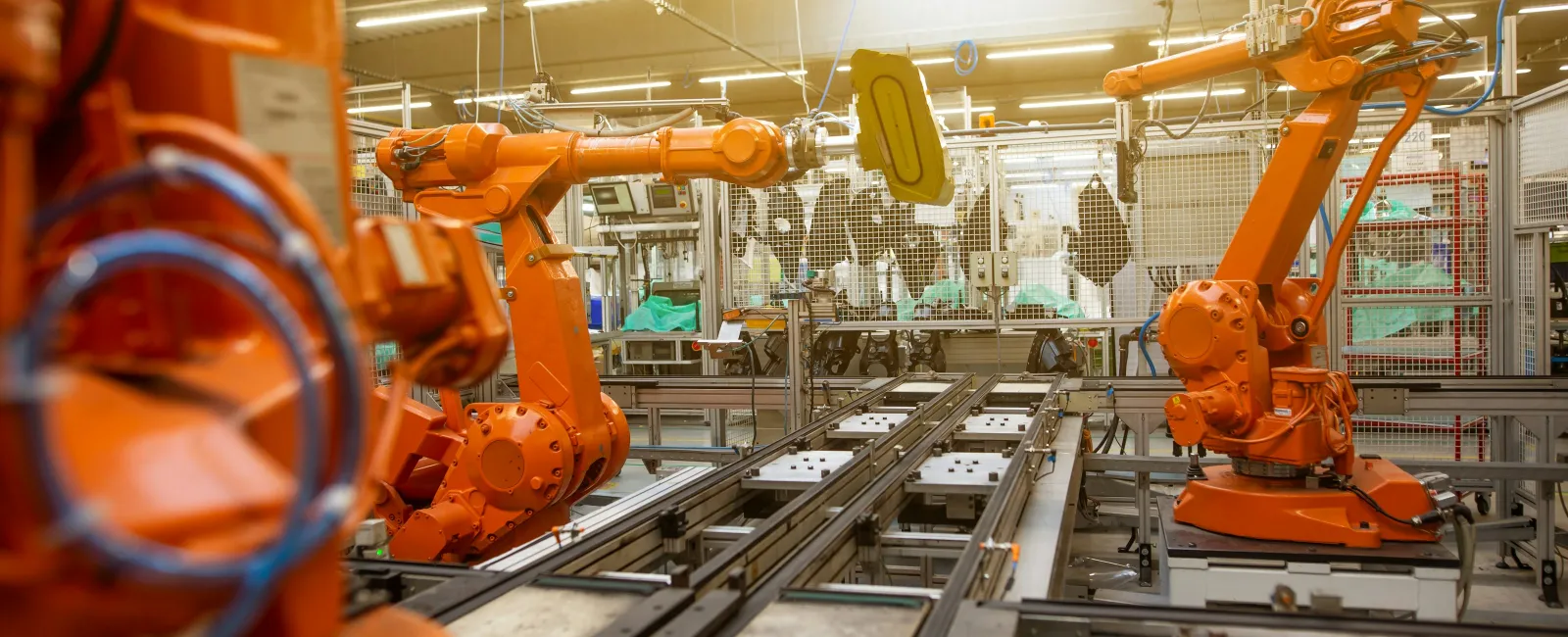 Industrial orange robotic arms working on automated assembly line in a bright factory setting.