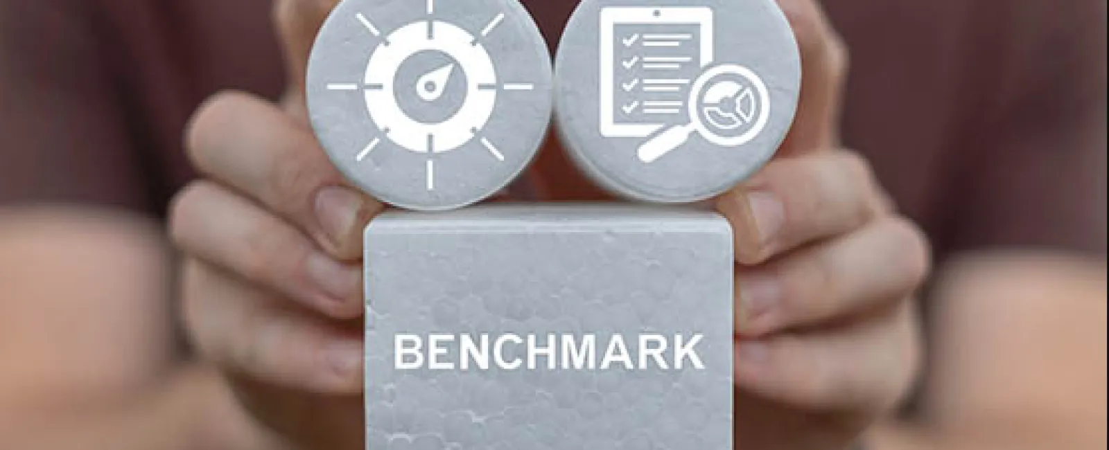 Hands holding blocks with benchmark text and icons of speedometer and checklist with magnifying glass.