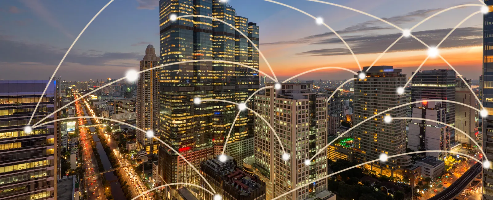 City skyline at sunset with illuminated skyscrapers and glowing network connections overlay