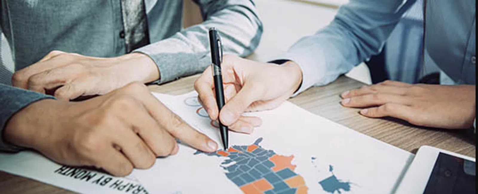 Two business professionals discussing a color-coded regional map on a table during a meeting.