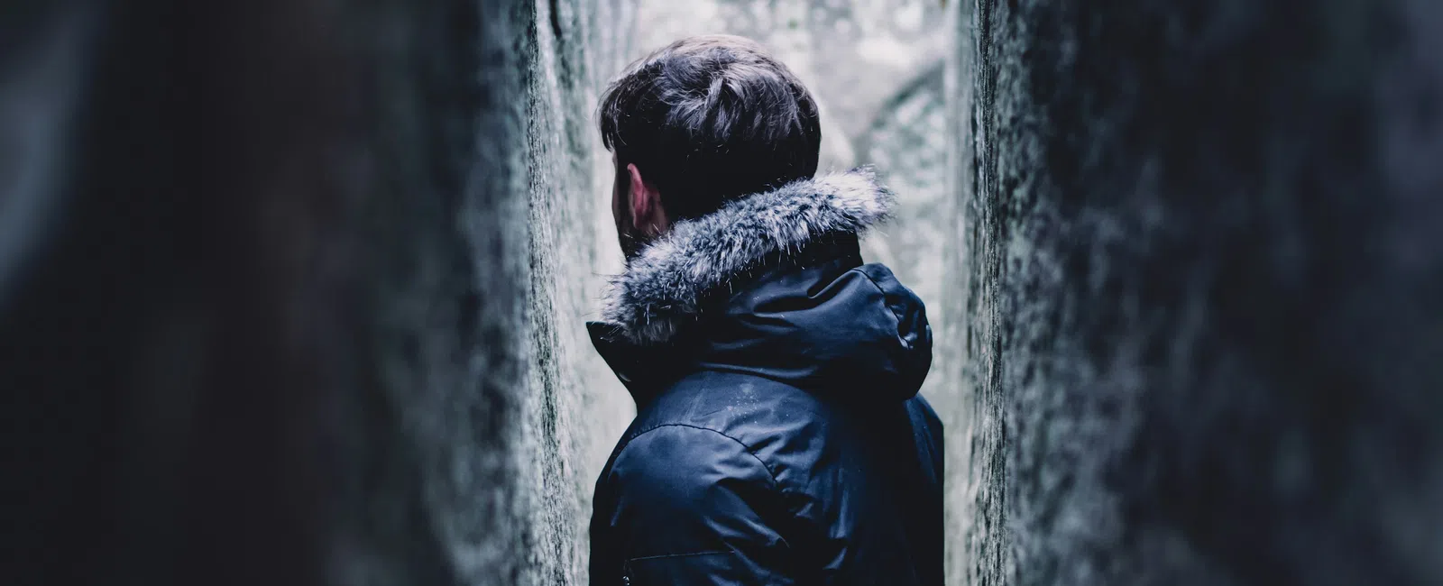 Person wearing black winter jacket standing between narrow rock walls in a natural outdoor setting.