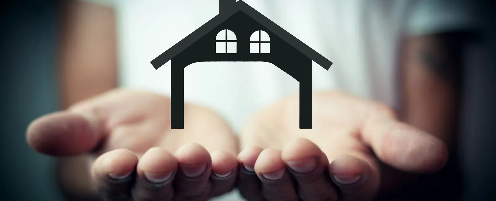 Person holding out hands with a black house icon floating above, symbolizing real estate or home protection